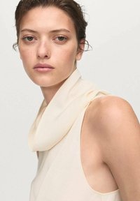 Cremfarbener ärmelloser Top mit drapiertem Hals. Leichter Stoff, weiche Textur und subtiler Glanz. Minimalistisches Design ohne sichtbare Muster.