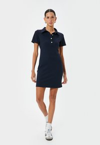 Granatowa sukienka polo wykonana z dzianiny, z kołnierzykiem, złotymi guzikami i dopasowanym krojem, stylizowana z białymi sneakersami.