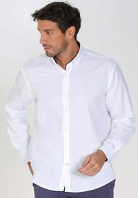 Chemise blanche à manches longues avec boutons, fabriquée en coton, dotée d'un col classique, d'une patte de boutonnage et d'une coupe ajustée. Texture douce et lisse.