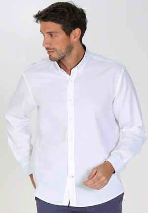 Chemise blanche à manches longues avec boutons, fabriquée en coton, dotée d'un col classique, d'une patte de boutonnage et d'une coupe ajustée. Texture douce et lisse.