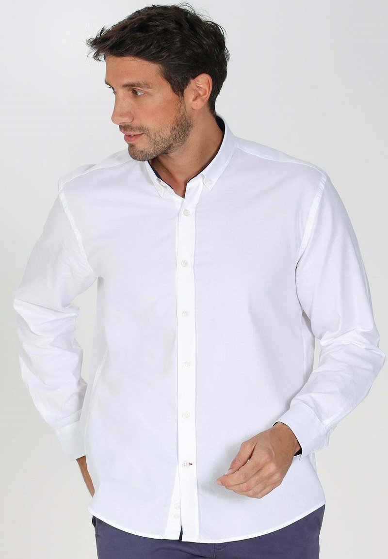Chemise blanche à manches longues avec boutons, fabriquée en coton, dotée d'un col classique, d'une patte de boutonnage et d'une coupe ajustée. Texture douce et lisse.