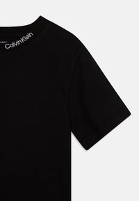 T-shirt en coton noir arborant un col rond et des manches courtes. Logo en broderie blanche au niveau du col. Texture lisse avec des coutures soignées.