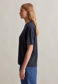 T-shirt noir marine à col rond, à manches courtes, coupe décontractée, texture douce, associé à un jean en denim bleu clair taille haute.