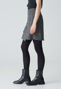 Grijze tweed rok met een subtiele textuur en een lichte asymmetrische ontwerp, gecombineerd met zwarte ondoorzichtige kousen en zwarte leren laarsjes tot de enkel.