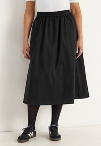 Black mid-length skirt with an elastic waistband and smooth texture, paired with black shoes featuring white stripes and dark tights.