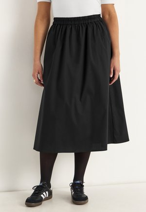 Schwarze mittellange Rock mit einem elastischen Bund und glatter Textur, kombiniert mit schwarzen Schuhen mit weißen Streifen und dunklen Strumpfhosen.