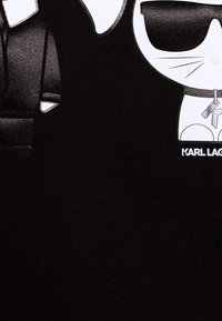 Tejido negro suave con un diseño gráfico que presenta un gato de dibujos animados con gafas de sol, complementado por el nombre de la marca "KARL LAGERFELD" en texto blanco.