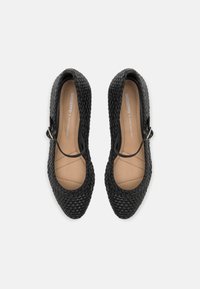 Bailarinas trenzadas negras con una plantilla de color beige claro. Presentan una puntera redondeada y una correa con una pequeña hebilla metálica. Exterior texturizado.