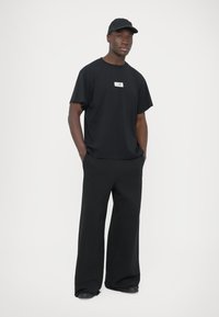 Μαύρο βαμβακερό t-shirt με μικρό λευκό λογότυπο, σε συνδυασμό με μαύρο παντελόνι φαρδύ στο πόδι. Το σύνολο ολοκληρώνεται με μαύρο καπέλο που ταιριάζει.