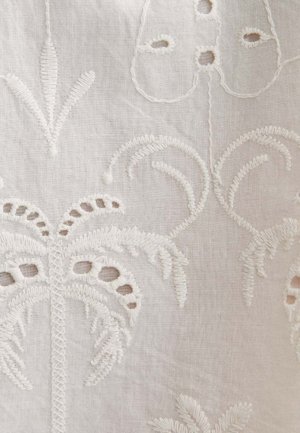 White fabric with intricate raised embroidery featuring floral and palm tree motifs, creating a delicate and textured pattern.