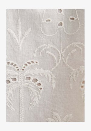 Tissu blanc avec une broderie en relief complexe présentant des motifs floraux et de palmiers, créant un motif délicat et texturé.