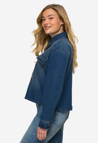Giacca di denim cropped di colore blu scuro, con colletto, taschino singolo sul petto e dettagli con bottoni; indossata con jeans blu chiaro.
