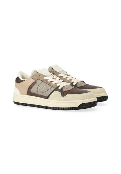 Un paio di sneaker basse con pannelli beige, marroni e crema, lacci bianchi e suole in gomma nera testurizzata su uno sfondo bianco.
