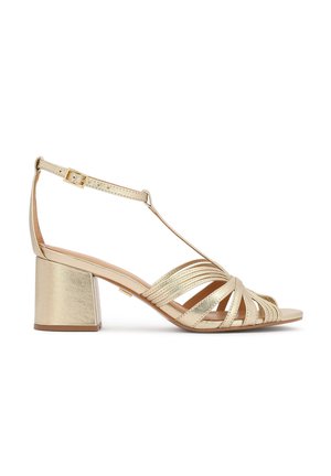 Auksinės bloko kulno basutės su keliomis kryžminėmis dirželiais. Turi sagties tipo dirželį prie kulkšnies ir metalinį blizgesį. Lygus paviršius, atvira priekinė dalis.