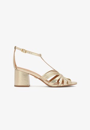 Auksinės bloko kulno basutės su keliomis kryžminėmis dirželiais. Turi sagties tipo dirželį prie kulkšnies ir metalinį blizgesį. Lygus paviršius, atvira priekinė dalis.