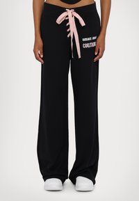 Zwarte wide-leg sweatpants met een roze satijnen trekkoord en een "Versace Jeans Couture" graphic aan de zijkant. Zacht materiaal en een ontspannen pasvorm.