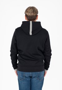 Schwarzer Kapuzenpullover mit subtilen Streifendetails an der Kapuze und den Bündchen, aus weichem Material und mit einer lockeren Passform. Tragen mit blauen Jeans.