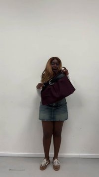 Mørkerød taske med et stort sort bælte og spænde, med en glat tekstur og rektangulær form, båret af en person i en denimnederdel.