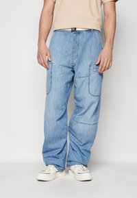 Svetlo modri denim hlače s cargo krojem in sproščenim fitom, z bočnimi žepi in črnim pasom. V kombinaciji z belimi supergami.