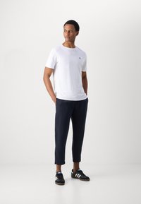 Witte t-shirt met korte mouwen, marineblauwe cropped broek en zwarte sneakers met witte strepen. Casual outfit met een relaxte pasvorm en minimalistisch design.