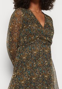 Robe portefeuille transparente à imprimé animalier avec des nuances de marron, bleu et noir. Elle présente un profond décolleté en V et des manches longues et fluides.