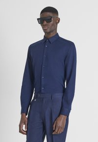 Camicia a maniche lunghe blu navy in tessuto leggero con bottoni, abbinata a pantaloni coordinati e occhiali da sole neri oversize.