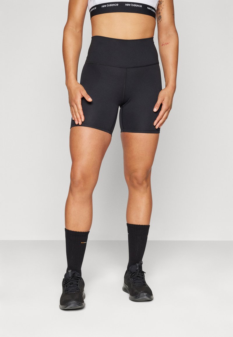 Calças de bicicleta pretas de cintura alta em um tecido suave com uma silhueta ajustada. Combinadas com meias e sapatos desportivos pretos.