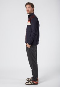 Navy zip-up jacket with color block design featuring cream, orange, and burgundy sections, paired with slim-fit gray pants and patterned sneakers.