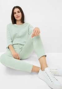Camicia a maniche lunghe a righe di colore verde menta abbinata a jeans slim-fit verde menta. Sneakers bianche con lacci e anelli argentati sulle dita.