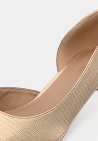 Χρυσό ψεύτικο δερμάτινο παπούτσι με επίπεδη σόλα και υφή που μοιάζει με δέρμα φιδιού. Διαθέτει στρογγυλεμένη μύτη και λείο εσωτερικό επένδυση.