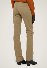 Pantalones ajustados color caqui, confeccionados en una mezcla de algodón, con cintura de altura media, dos bolsillos traseros y un acabado limpio, combinados con botas negras de tacón cuadrado.