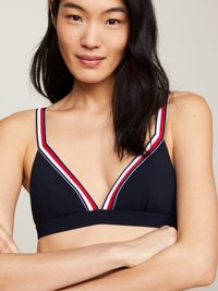 Bralette triangolare blu navy con scollatura a V profonda, caratterizzato da accenti a strisce bianche e rosse lungo i bordi. Texture liscia, senza imbottitura.
