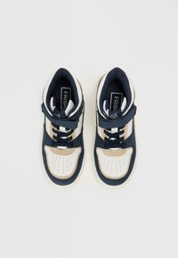 Korkokenkä, jossa on tummansininen ja valkoinen nahkapinta, pehmeä kaulus, rei'itetty varvasosa ja siniset nauhat. Hiusmerkki on kielessä.