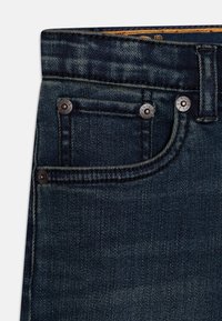Dark blue denim jeans feature a classic design with a front pocket and rivet detailing. The texture is smooth with subtle fading.