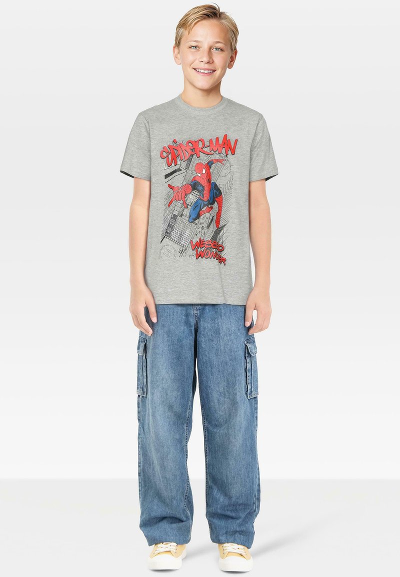 Γκρι βαμβακερό t-shirt με γραφικό του Spider-Man σε κόκκινο και μπλε, συνδυασμένο με ανοιχτό μπλε cargo σορτς και κίτρινα αθλητικά παπούτσια.