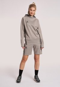 Conjunto atlético de color gris claro que incluye una camiseta de manga larga con capucha y pantalones cortos, con detalles y logotipos negros en ambas piezas.