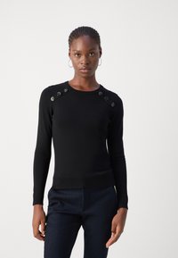 Černý svetr s dlouhými rukávy, žebrovanou texturou a dekorativními ozdobami na ramenou. Úzký střih s kulatým výstřihem.