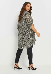 Kimono trasparente bianco e nero con un motivo ondulato, design fluido e maniche ampie, abbinato a leggins neri e scarpe con tacco.