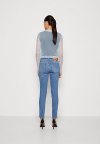 Top de gasa azul claro con mangas cortas, combinado con jeans ajustados de denim desgastado y zapatos de tacón negro. Etiqueta destacada en los jeans.