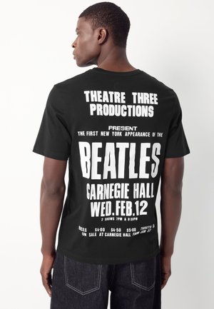 Schwarzes T-Shirt mit großen, fetten weißen Text auf der Rückseite. Der Text enthält die Veranstaltungsdetails für ein Beatles-Konzert in der Carnegie Hall.
