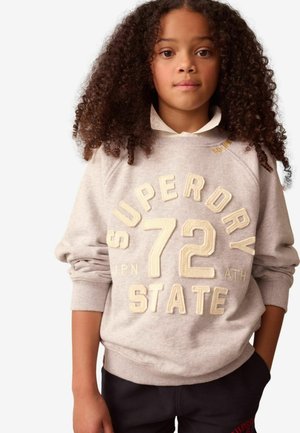 Világosszürke pulóver, krémszínű, dombornyomott "SUPERDRY 72 STATE" felirattal. Bordázott mandzsetták és szegély. Sötét nadrággal párosítva.