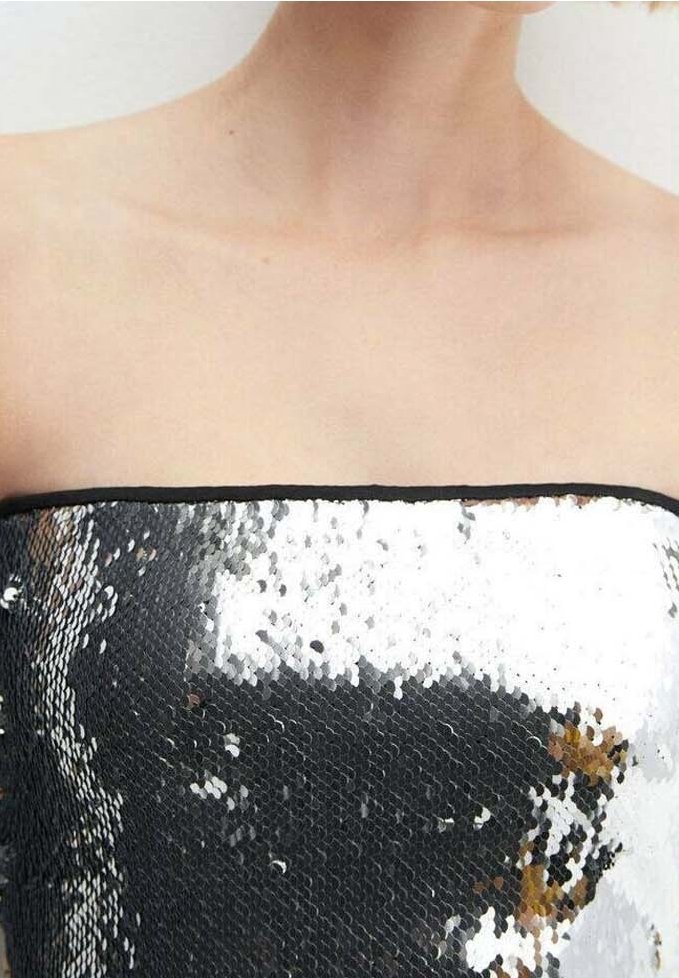 Femme portant un haut sans bretelles orné de sequins réversibles noirs et argentés, laissant visible la peau du cou jusqu'au haut de la poitrine.