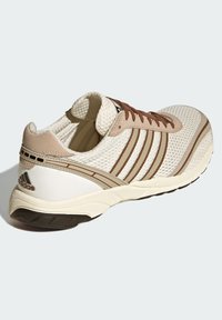 Ελαφρύ μπεζ αθλητικό παπούτσι με επάνω μέρος από δίχτυ, καφετί λεπτομέρειες και τρεις λεπτές ρίγες στο πλάι. Διαθέτει υφή στη σόλα για καλύτερη πρόσφυση.