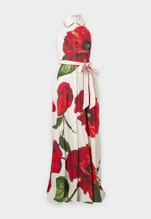 Femme portant une robe maxi blanche sans manches avec de grandes impressions de fleurs de coquelicot rouges et un col, debout les mains dans les poches.