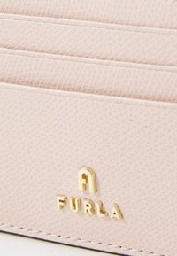 Svijetlo ružičasti kožni novčanik s više pretinaca za kartice, s zlatnim utisnutim logotipom "FURLA" i kontrastnim šavovima duž rubova.