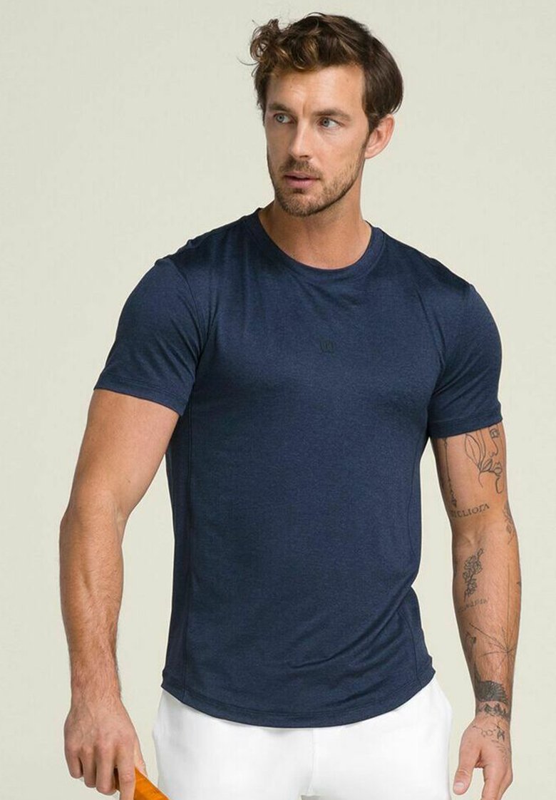 Camiseta deportiva de manga corta en azul marino, con forma ajustada, textura de tejido suave, con un sutil logo en el pecho, combinada con pantalones cortos blancos.
