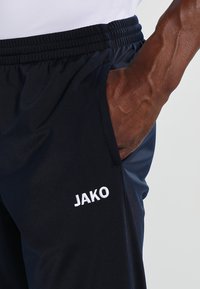 Marineblauwe sportshorts met een elastische tailleband en zijzak; voorzien van een witte geborduurde "JAKO"-logo. Het materiaal is glad en lichtgewicht.