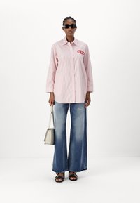 Striped pink button-up shirt with long sleeves and a logo, paired with flared blue jeans, black sandals, and a small beige handbag.