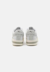 Fehér bőr sportcipők szürke részletekkel, velúrból készült sarokrésszel, puha béléssel és texturált talppal. Puma logó a hátsó részen.