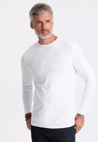 Vit långärmad skjorta i mjukt tyg med rund halsringning. Har en figurnära design och minimalistisk stil, i kombination med mörka jeans.